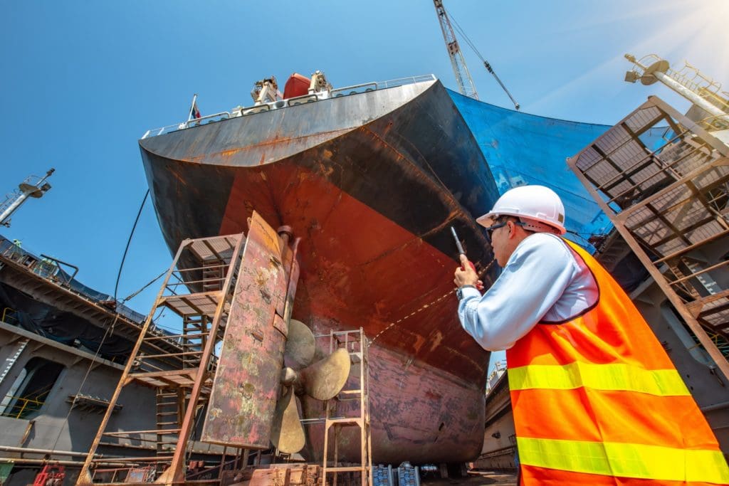 Port Master, surveyor inspecting the bulkhead of commercial cargo ship in floating dry dock, recondition of overhaul repairing and painting, sand blasting, or cold spray repair in dry dock yard